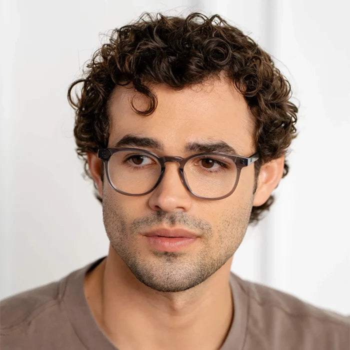 Crystal Grey || Close up of round prescription glasses with grey acetate frame and clear lens worn by man with curly hair indoors