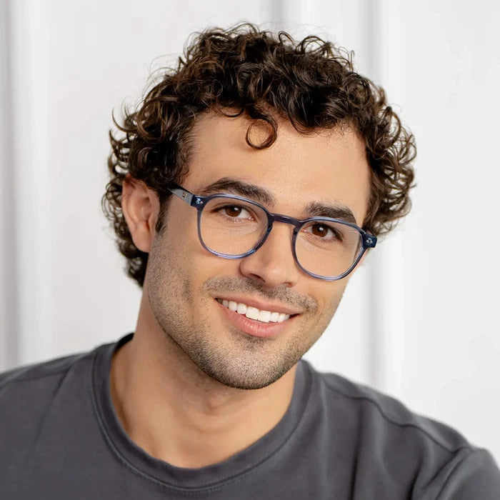 Pacific Blue || Square prescription glasses with blue frame and clear lens worn by a smiling man with curly hair indoors