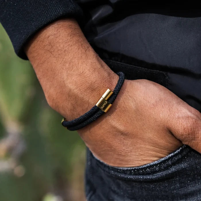 Onyx Black / Gold || Close up of the 14K Gold Plated Adjustable Pull Closure Black Rope Bracelet on a man’s wrist outdoors