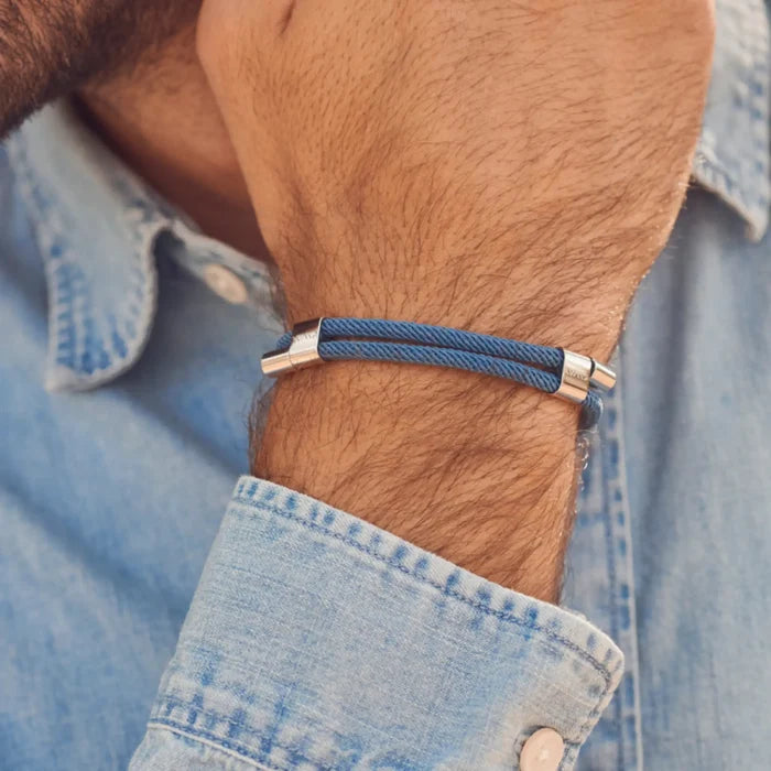 Denim Blue / Silver || Close up view of the Silver Stainless Steel Adjustable Pull Closure Blue Rope Bracelet on a man's wrist in natural lighting.