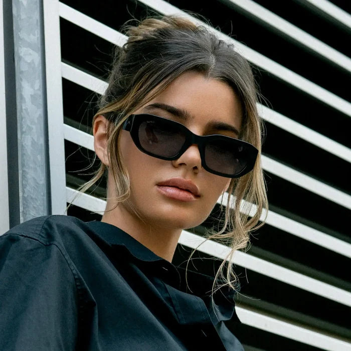 Black / Grey || Thick rectangular sunglasses with bold acetate frames and dark tinted lenses featuring a straight bridge worn by a woman outdoors in natural light