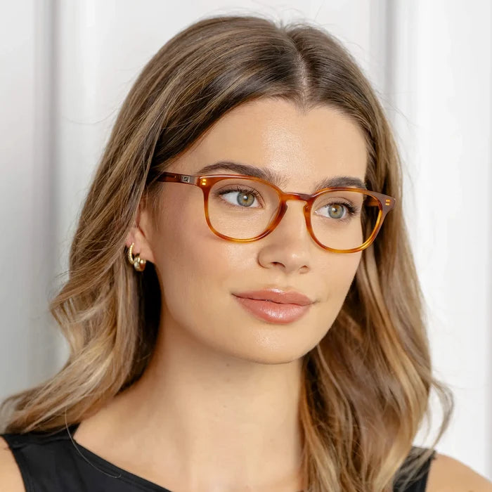 Honey Tortoise || Miles blue light glasses with translucent honey tortoise round frames worn by woman with wavy hair in soft lighting