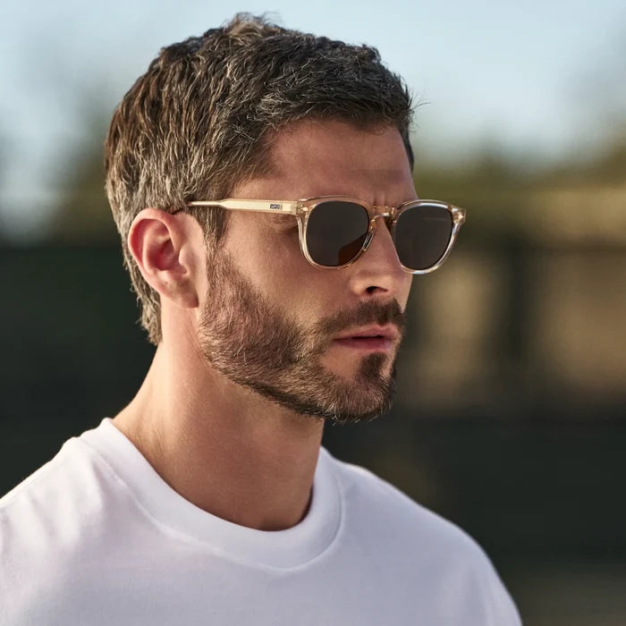 Man wearing Round Sunglasses with Sand Brown Frame and Dark Brown Oval Lens outdoors