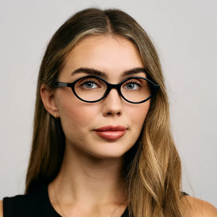 Black || Oval prescription eyeglasses with slim black frame worn by woman indoors in natural light