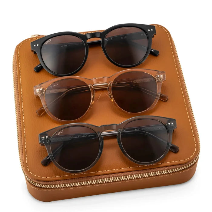 Brown Case || Three pairs of round frame sunglasses arranged on a brown zippered leather case with white stitching details